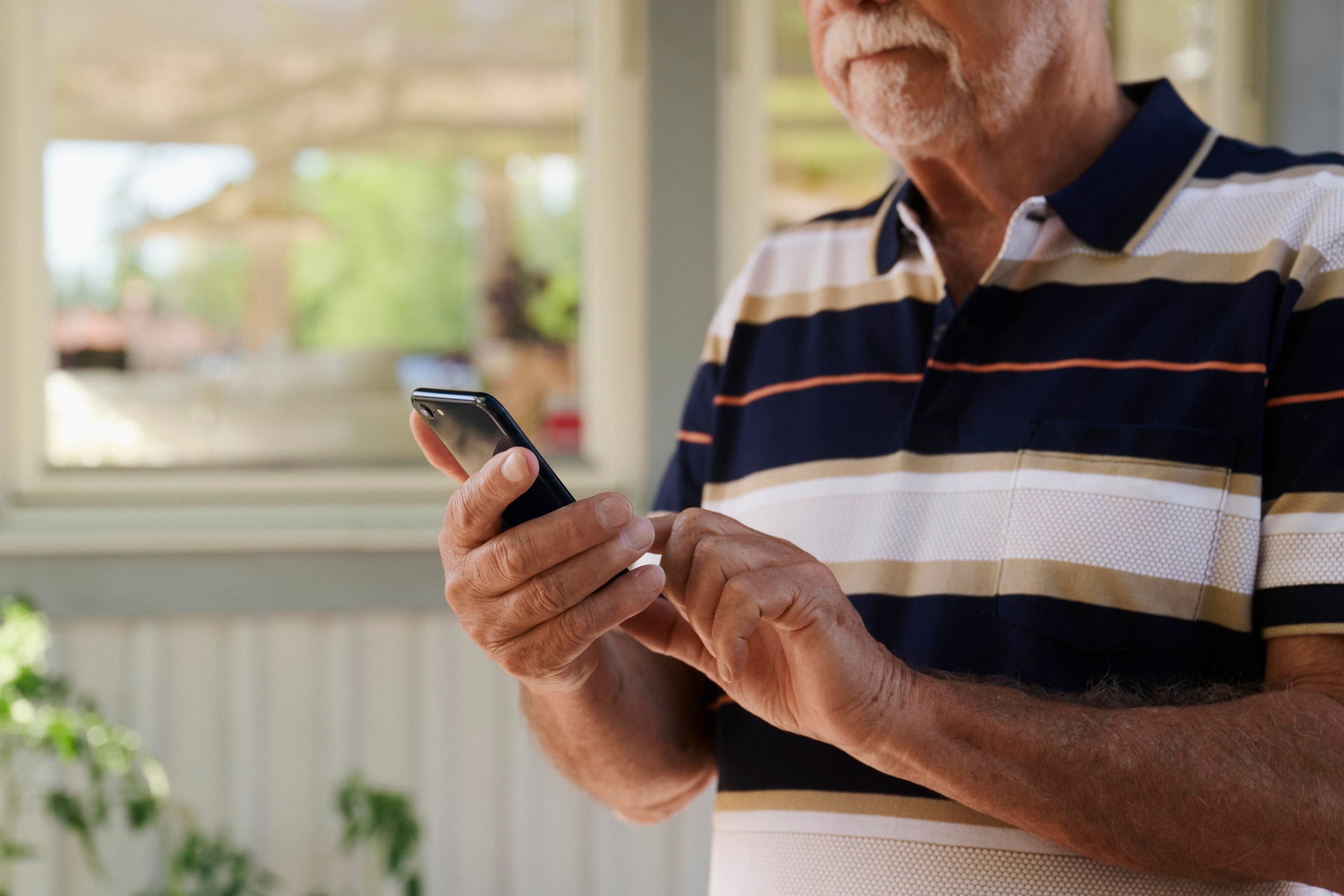 Närbild på en äldre man som scrollar på sin mobil